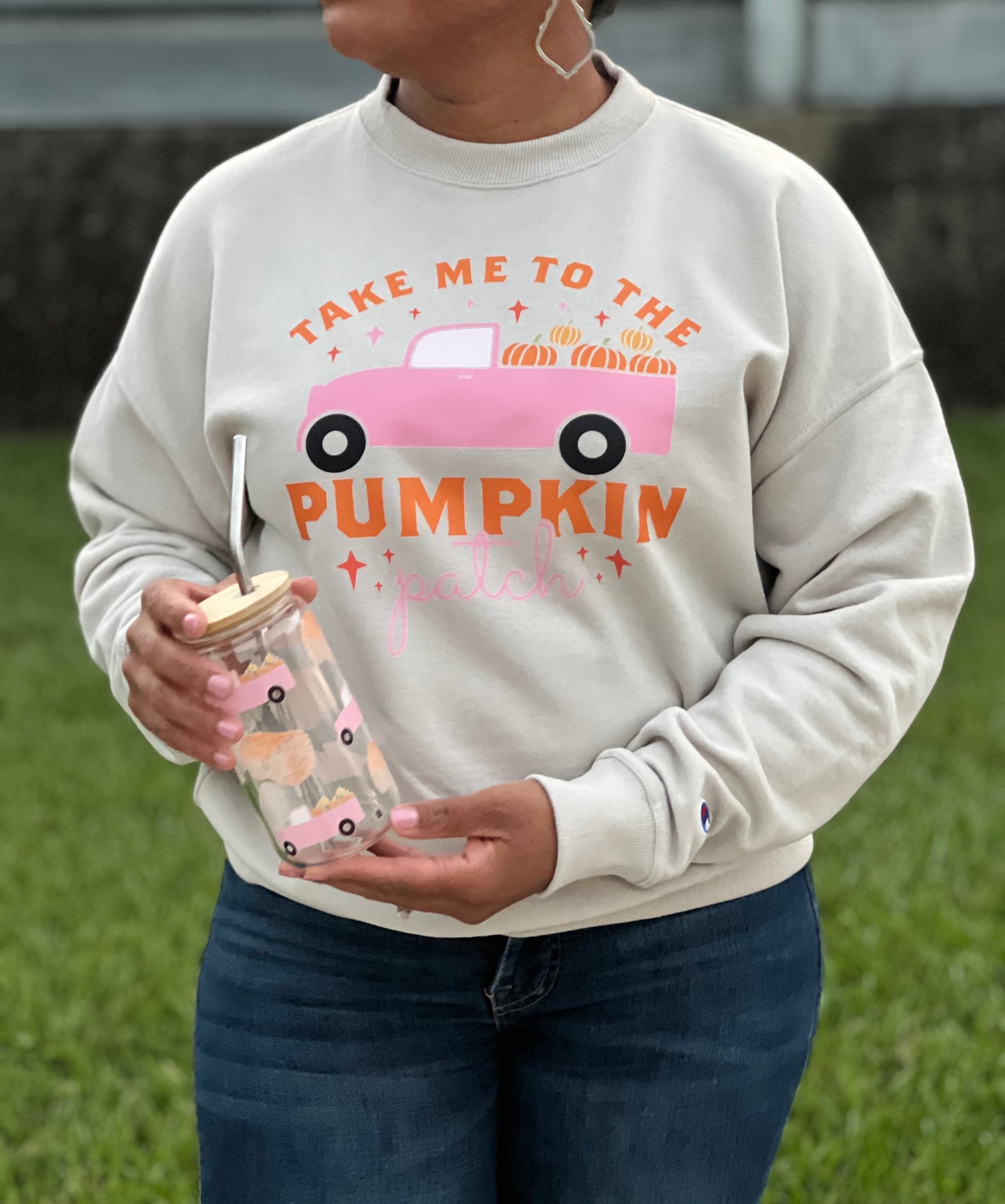 A woman wearing a crewneck sweatshirt with a pink truck and the saying Take Me to the Pumpkin Patch in orange text.