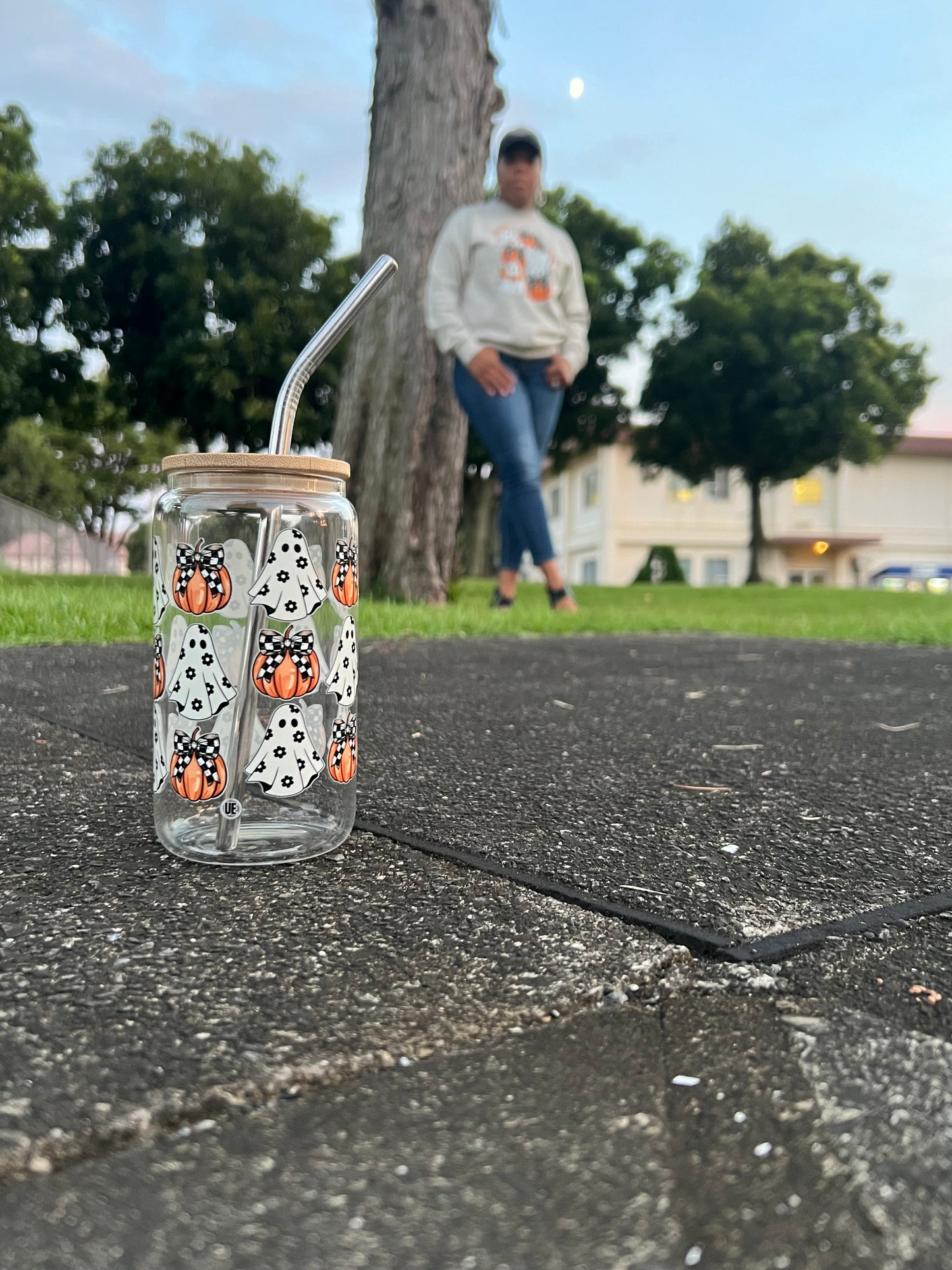A halloween glass can embellished with ghosts and pumpkins, checker-print bows, has a bamboo lid and metal straw.