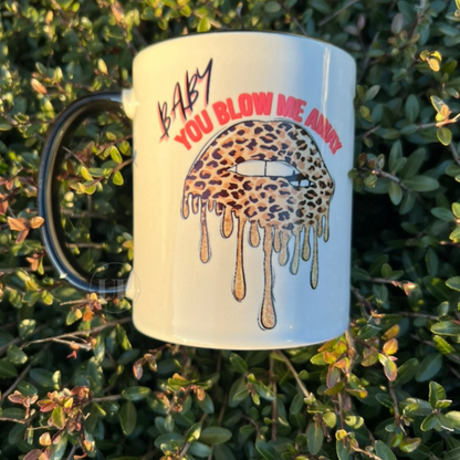 An 11oz white ceramic mug with black handle and interior with Baby you blow me away test on the front and an image of cheetah print lips.